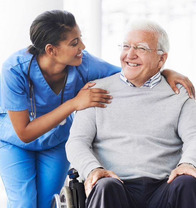 A nurse is putting her arm around an older man in a wheelchair.