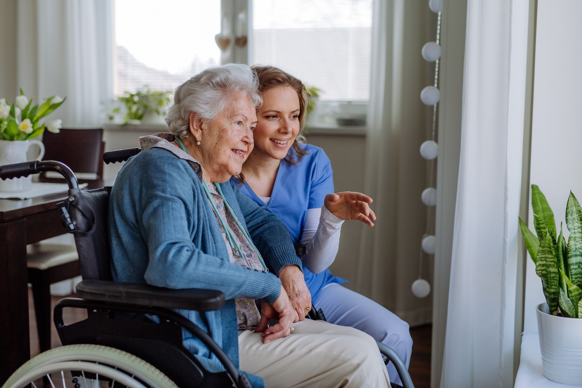 An elderly woman in a wheelchair is sitting next to a nurse.