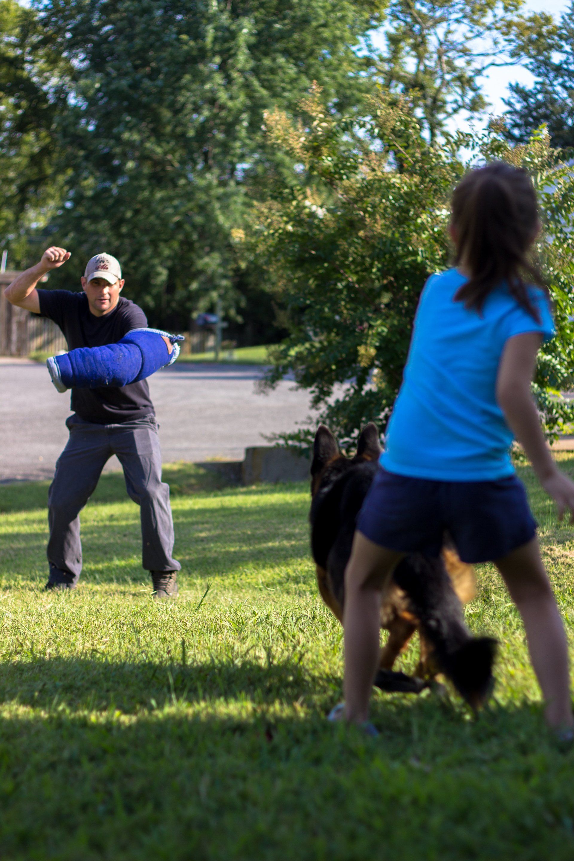 Two people play catch in a sunny park, one in a blue shirt and one holding a blue ball.
