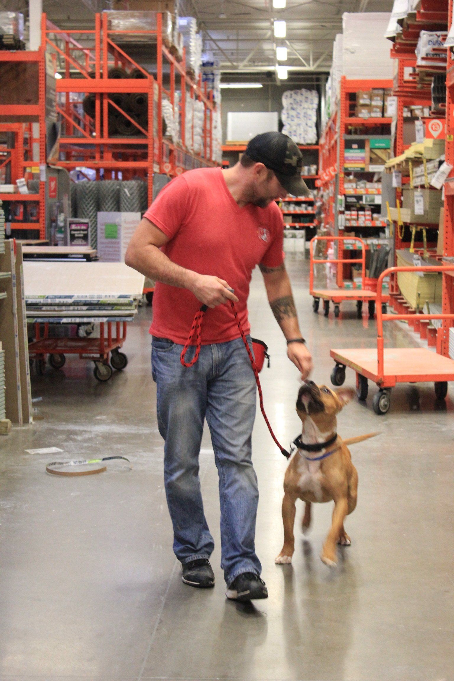Man in red shirt walking a dog on leash through a warehouse aisle