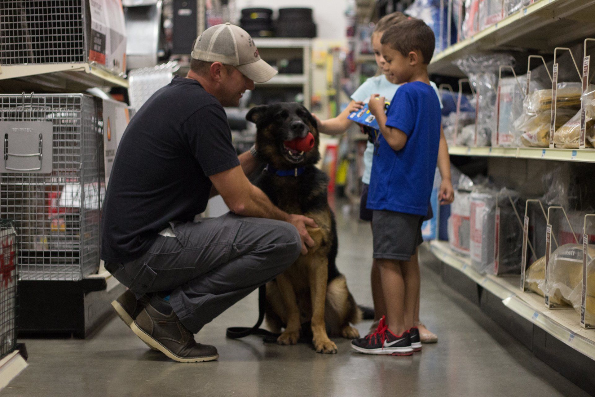 Man kneels beside a large dog while a boy stands nearby in a pet store aisle.
