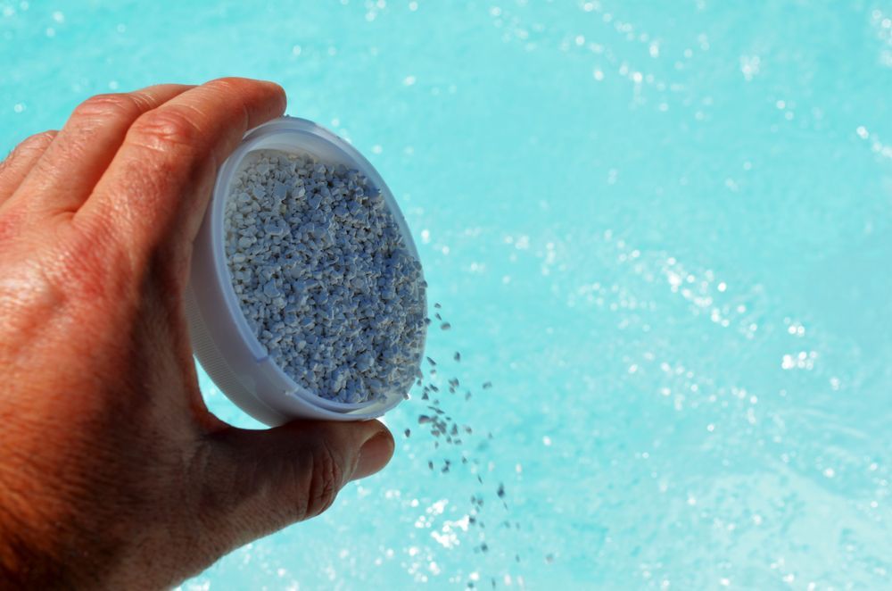Person Is Pouring Chemicals Into a Swimming Pool — Beaches Pool Supplies in Kewarra Beach, QLD