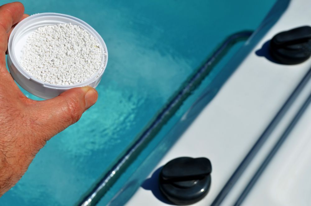 Person Is Holding a Container of Bleach Chemical in Front of A Swimming Pool — Beaches Pool Supplies in Kewarra Beach, QLD