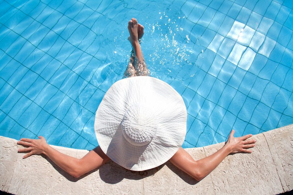 Woman in a white hat is laying on the edge of a swimming pool — Pool Cleaning in Clifton Beach, QLD