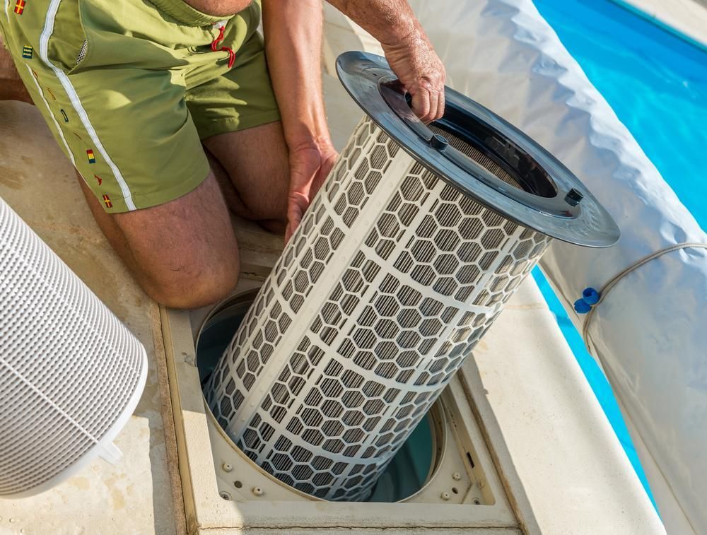 A Man Is Kneeling Down to Remove a Filter from A Swimming Pool — Beaches Pool Supplies in Kewarra Beach, QLD