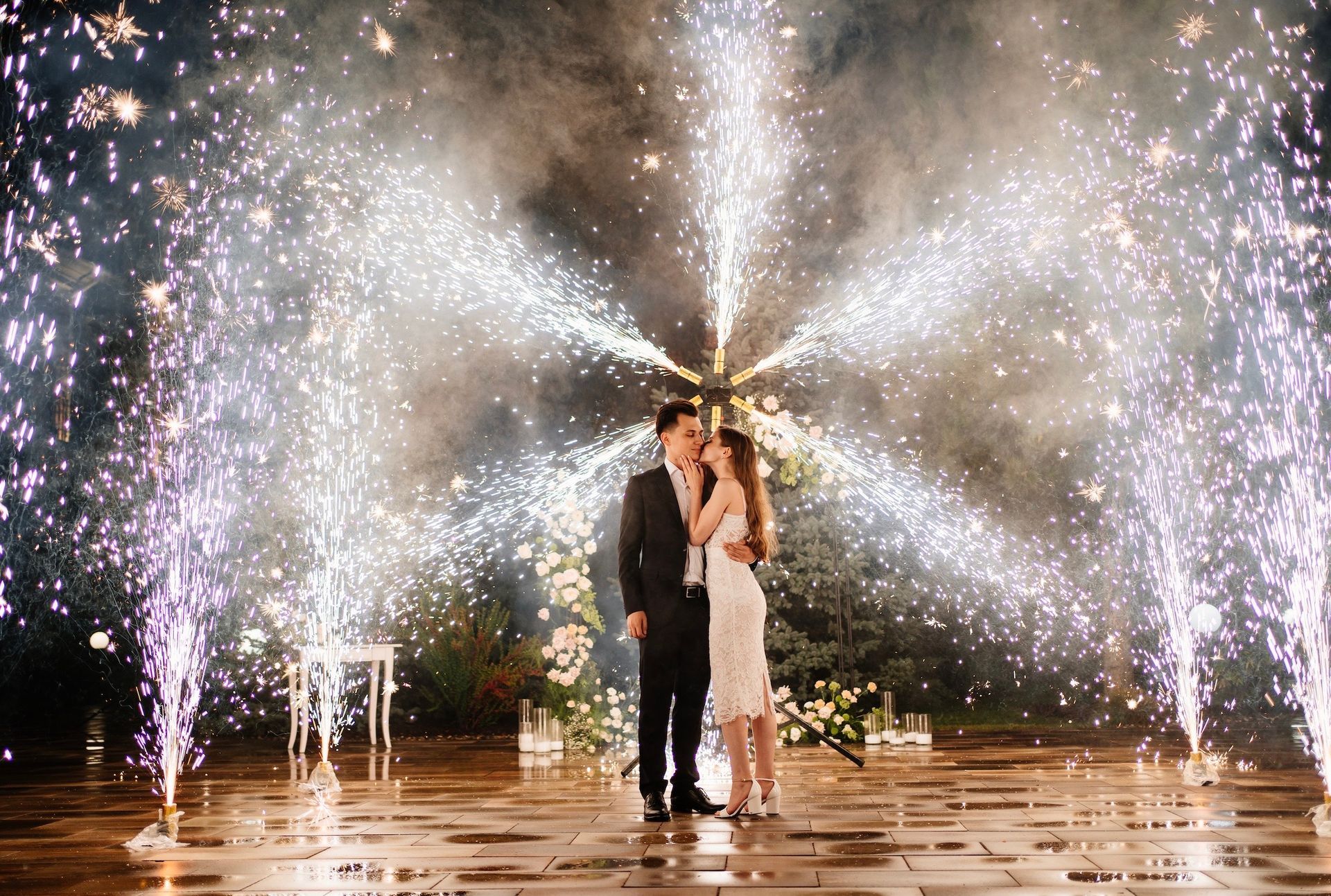 A bride and groom are standing in front of a fireworks display.