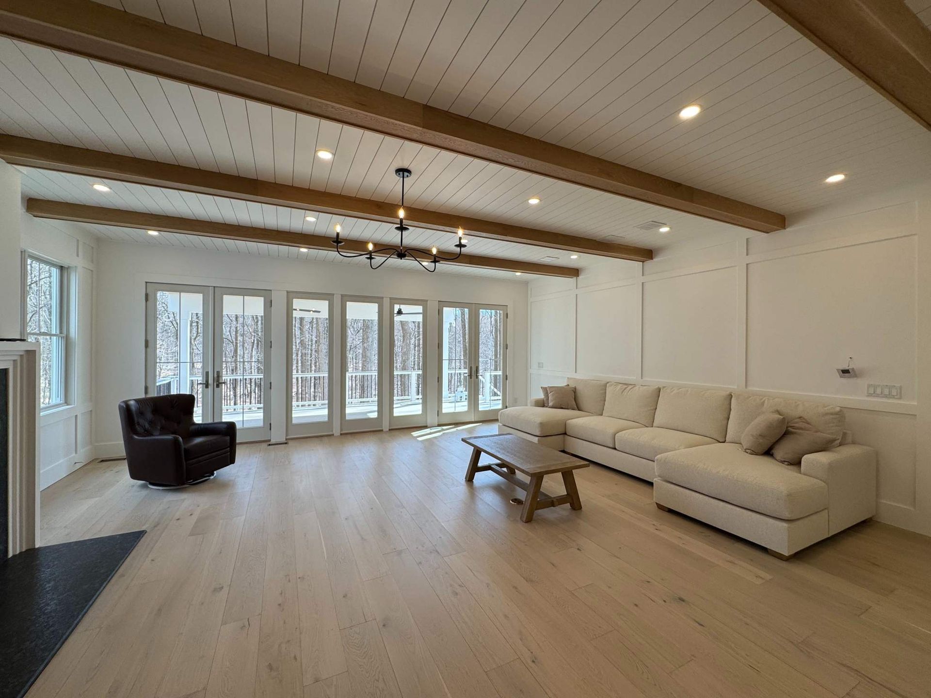 Living room with wood beam ceiling, light wood floors, large windows, and sectional sofa in a custom