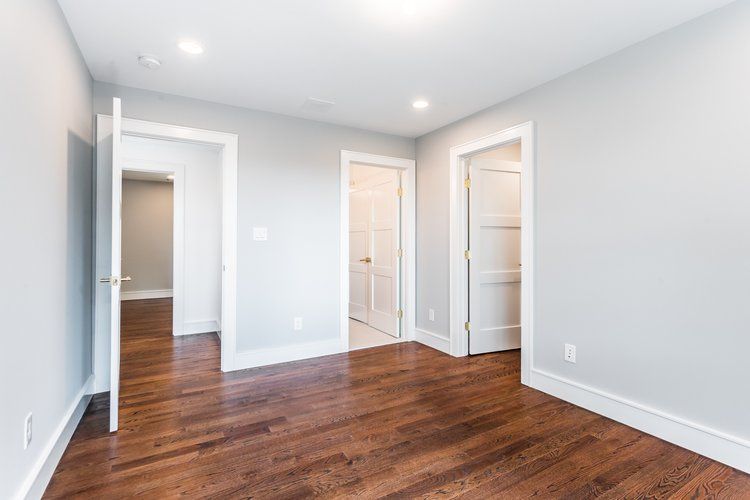 Empty room with hardwood floors, three white doors, and light gray walls.