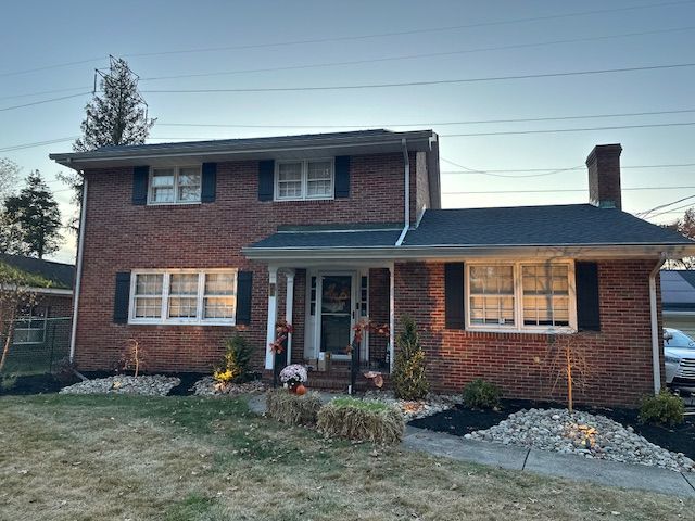 Brick two-story house with black shutters, chimney, and landscaped front yard with a walkway.