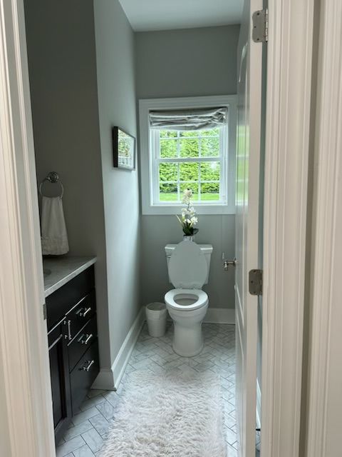 Small bathroom with toilet, sink, and window; gray walls, white trim, and light-colored floor.