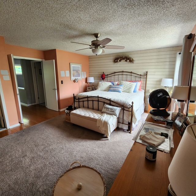 Bedroom with bed, dresser, orange and white walls, wood floor, and carpet.