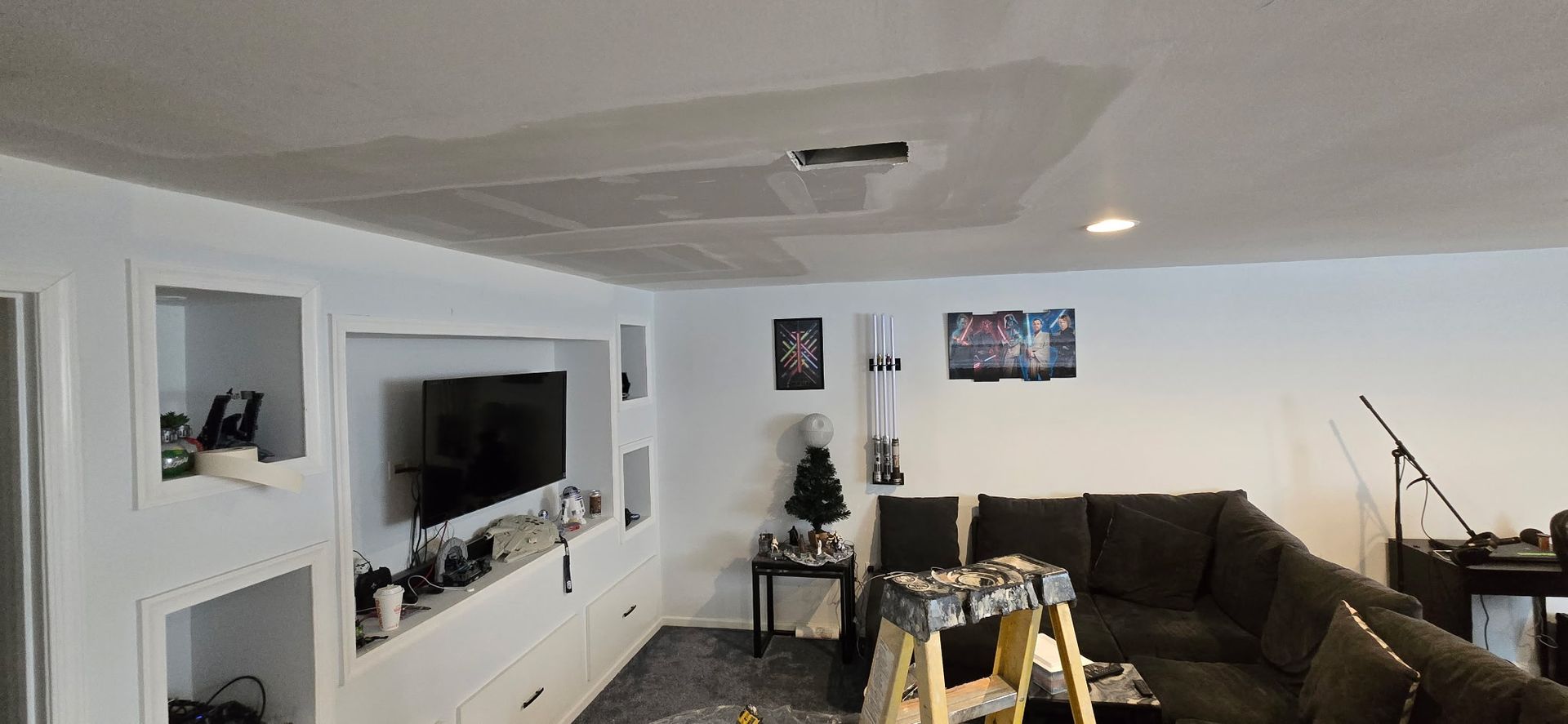 Living room with built-in TV, sectional sofa, and exposed ceiling repair.