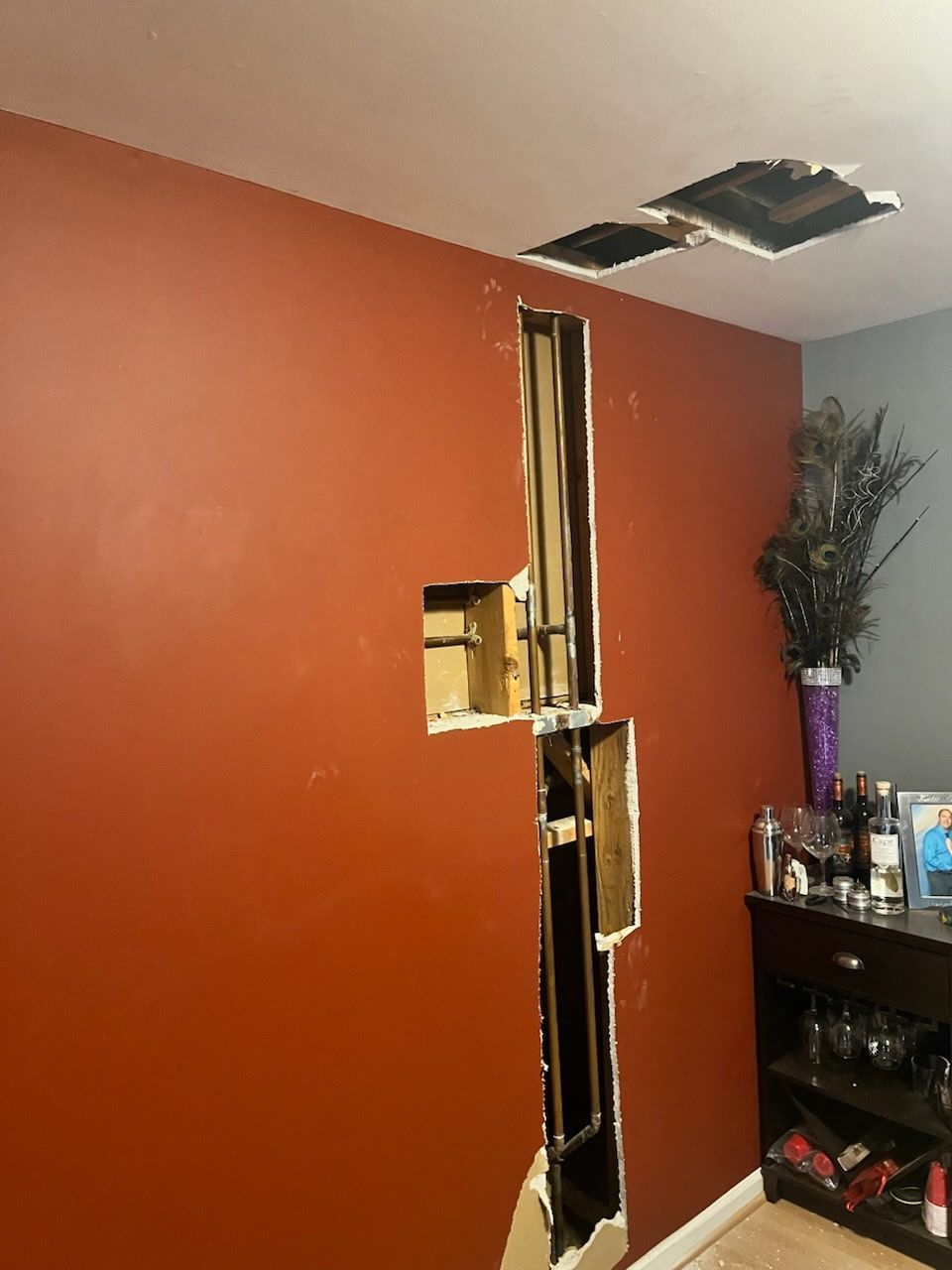 Red wall with large holes, exposed studs, and a damaged ceiling in a room.