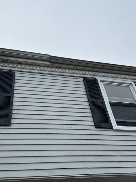 Exterior of a light gray house with black shutters and trim, under a gray sky.