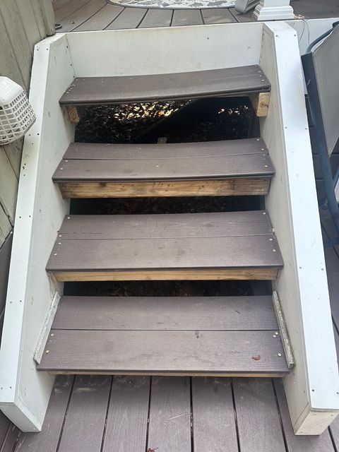 Exterior wooden stairs with damaged top step and a dark space beneath.