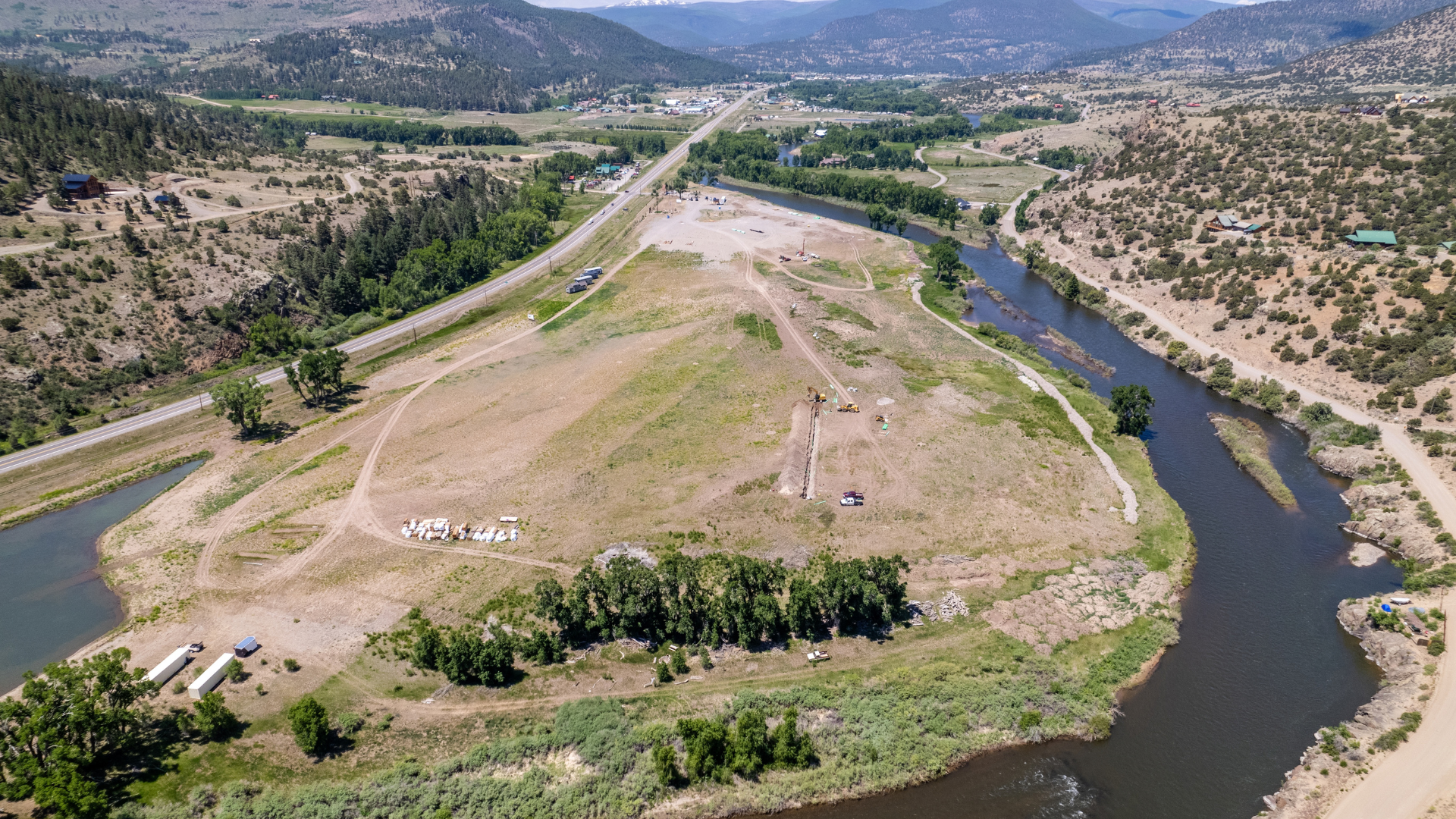Aerial view of a river winding past a grassy peninsula, road, and distant mountains at Rio Grande RV Resort
