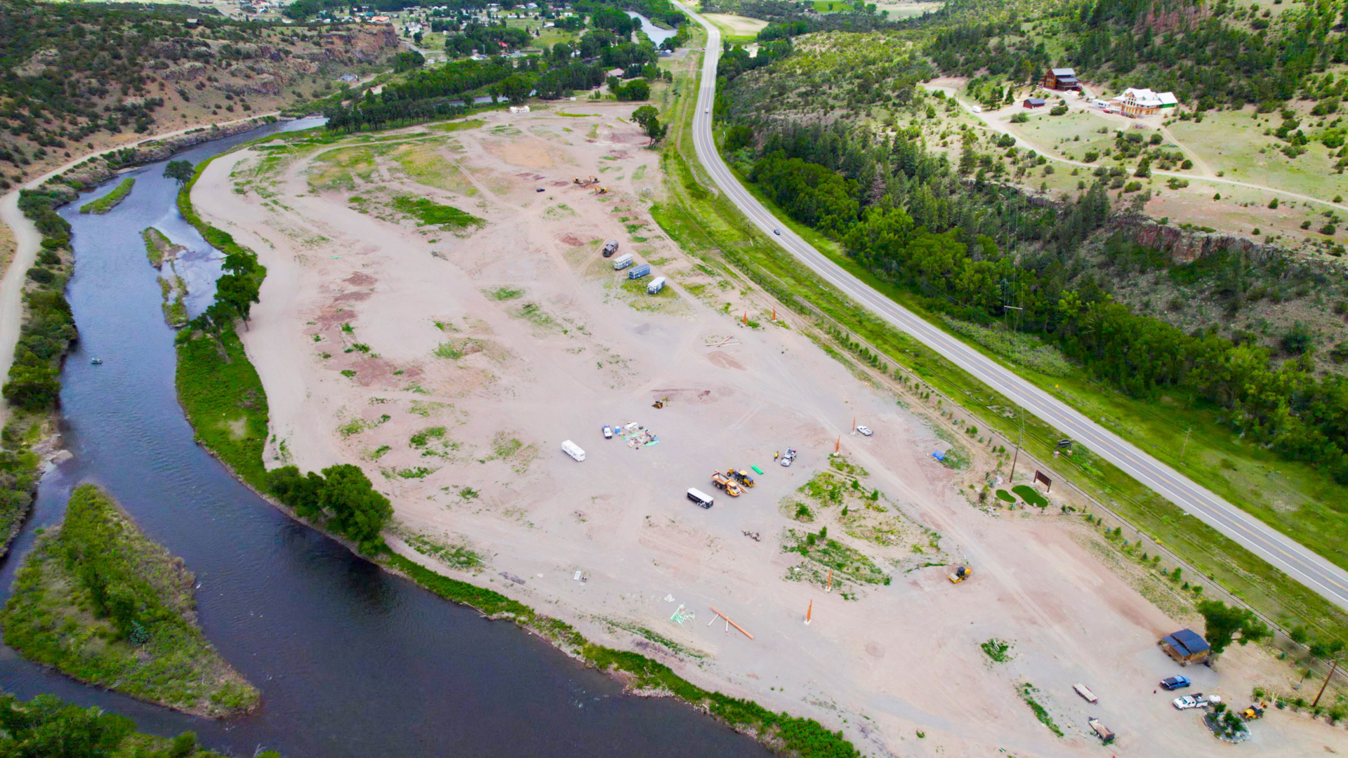 Aerial view of a river beside a sandy floodplain, green hillside, and a road curving through the landscape in Rio Grande RV Resort