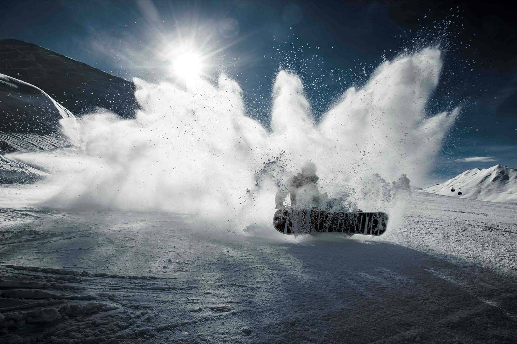 Snowboarder making a large cloud of snow on a sunny mountain.
