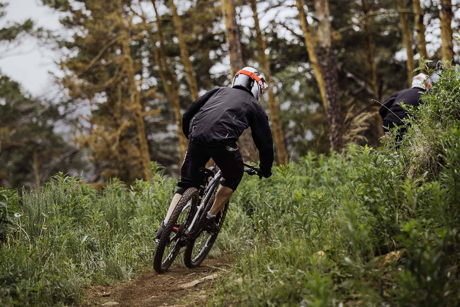 Mountain biker rides down a dirt trail in a forest, wearing a helmet and black jacket.