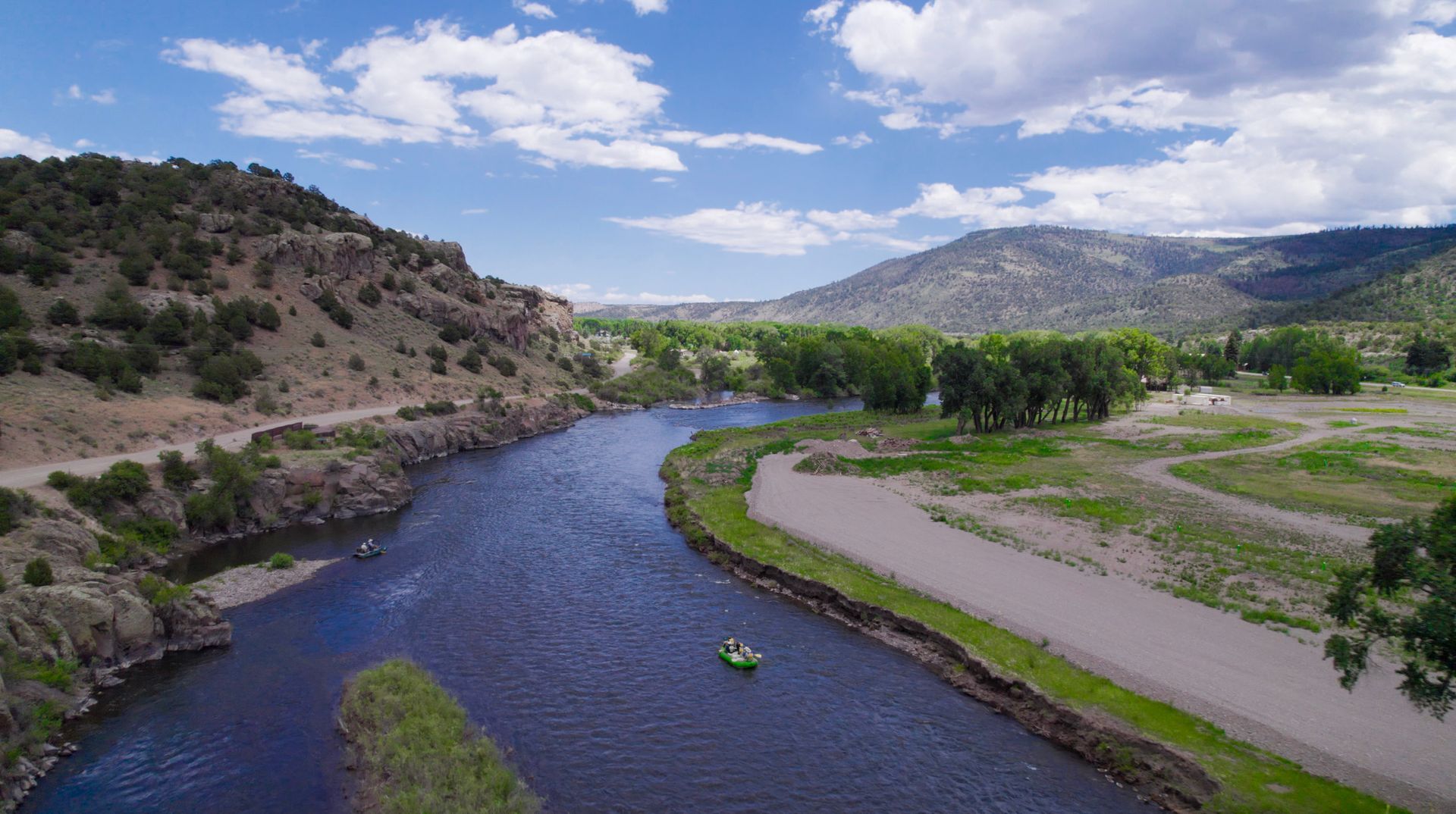 River winding through a green valley with hills, mountains, and a partly cloudy sky