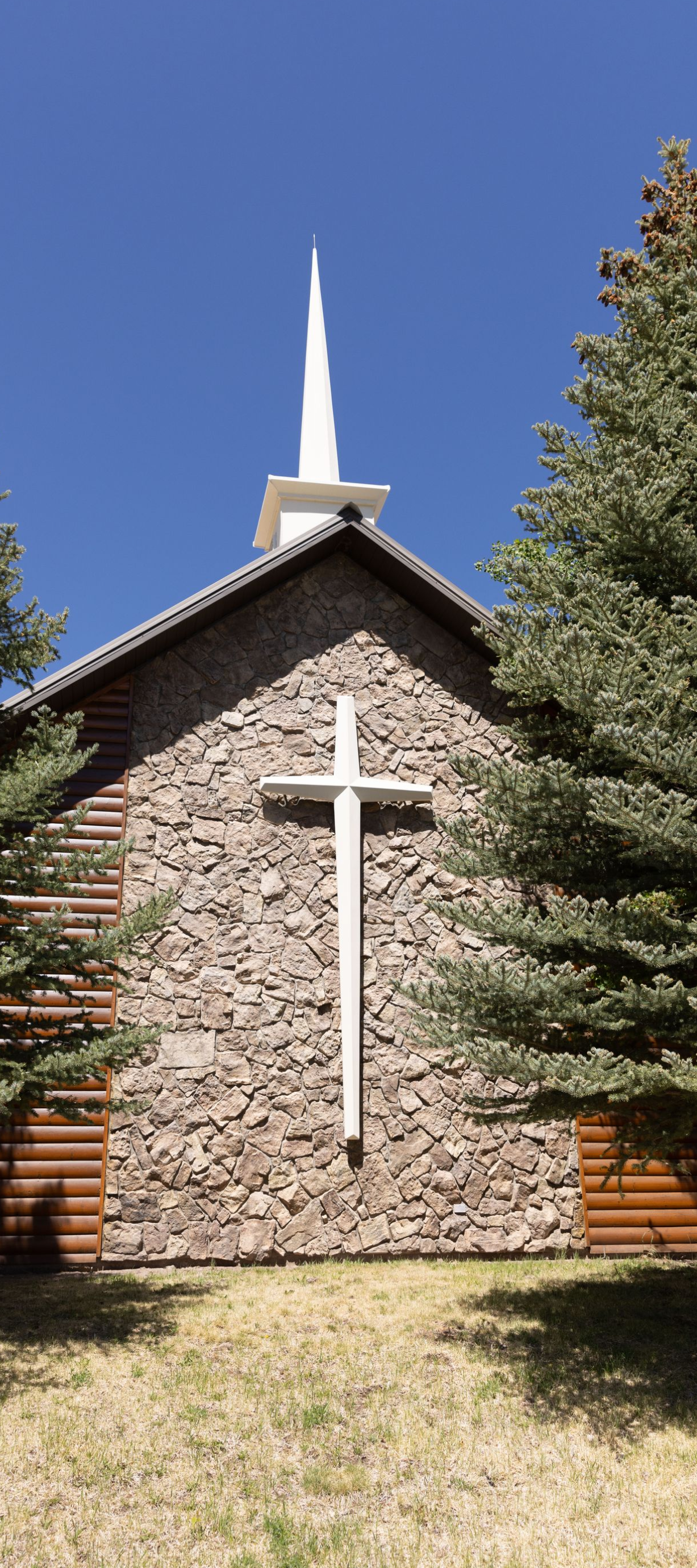 Stone church facade with white cross and steeple against a blue sky