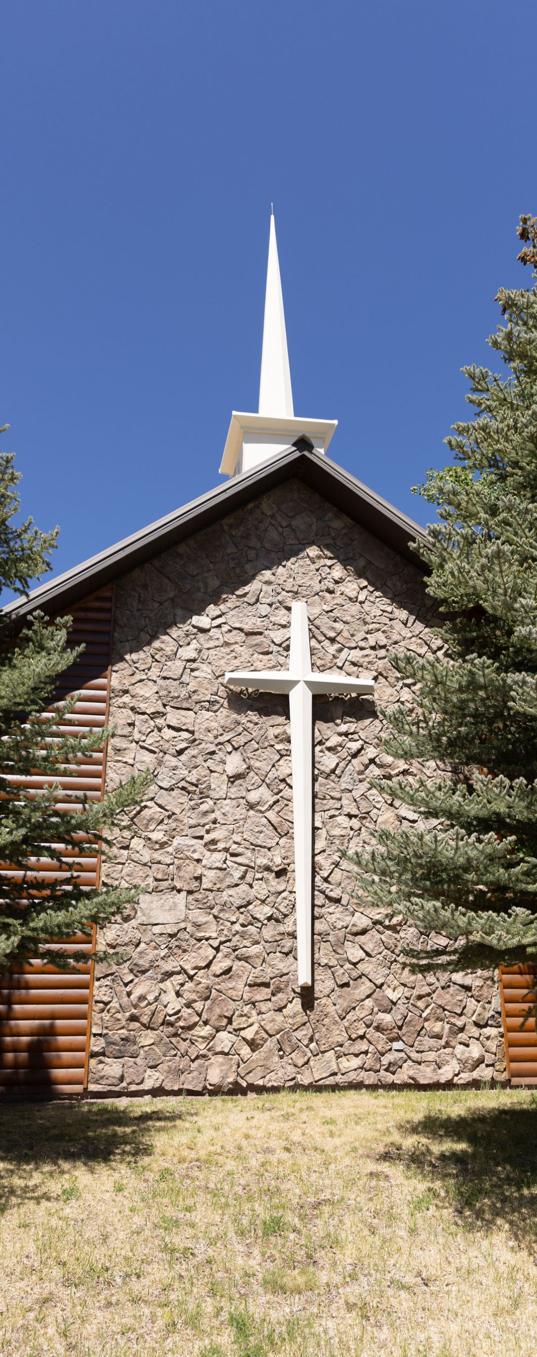 Stone church facade with a white cross and steeple against a blue sky