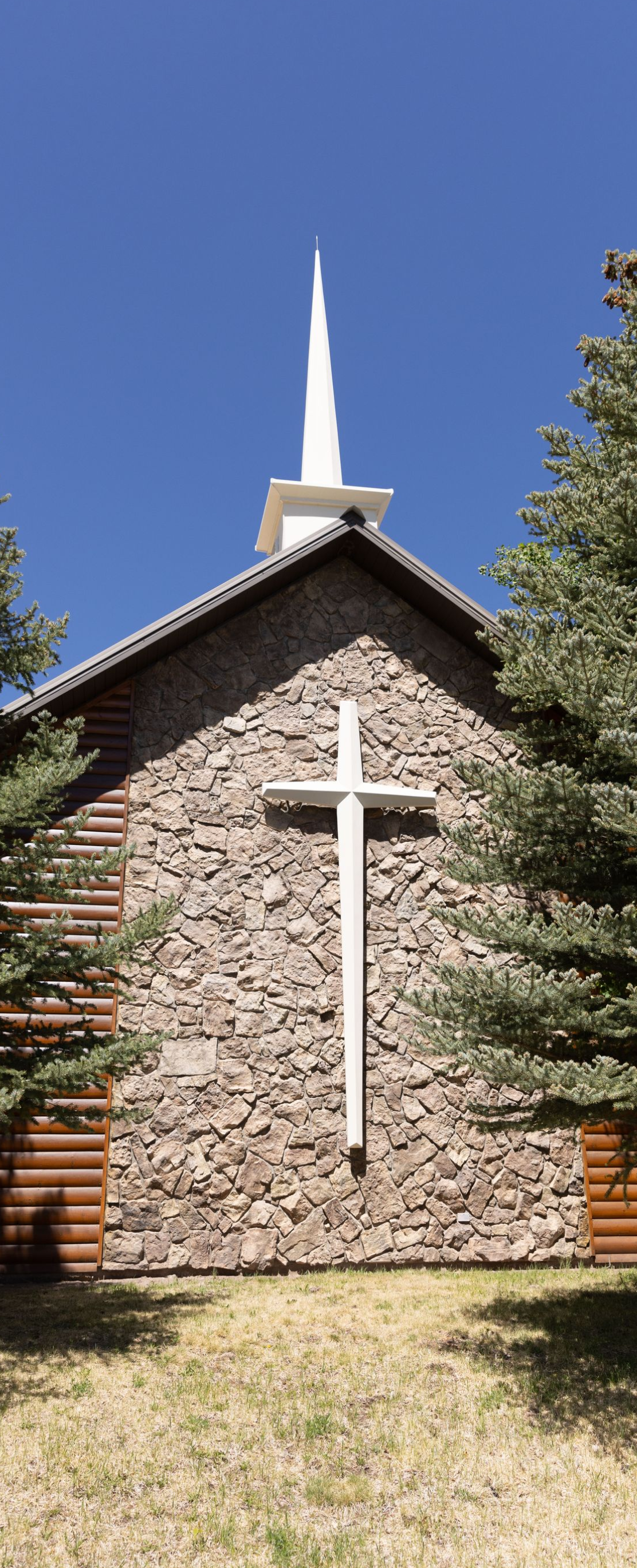 Stone church facade with white cross and steeple against a blue sky