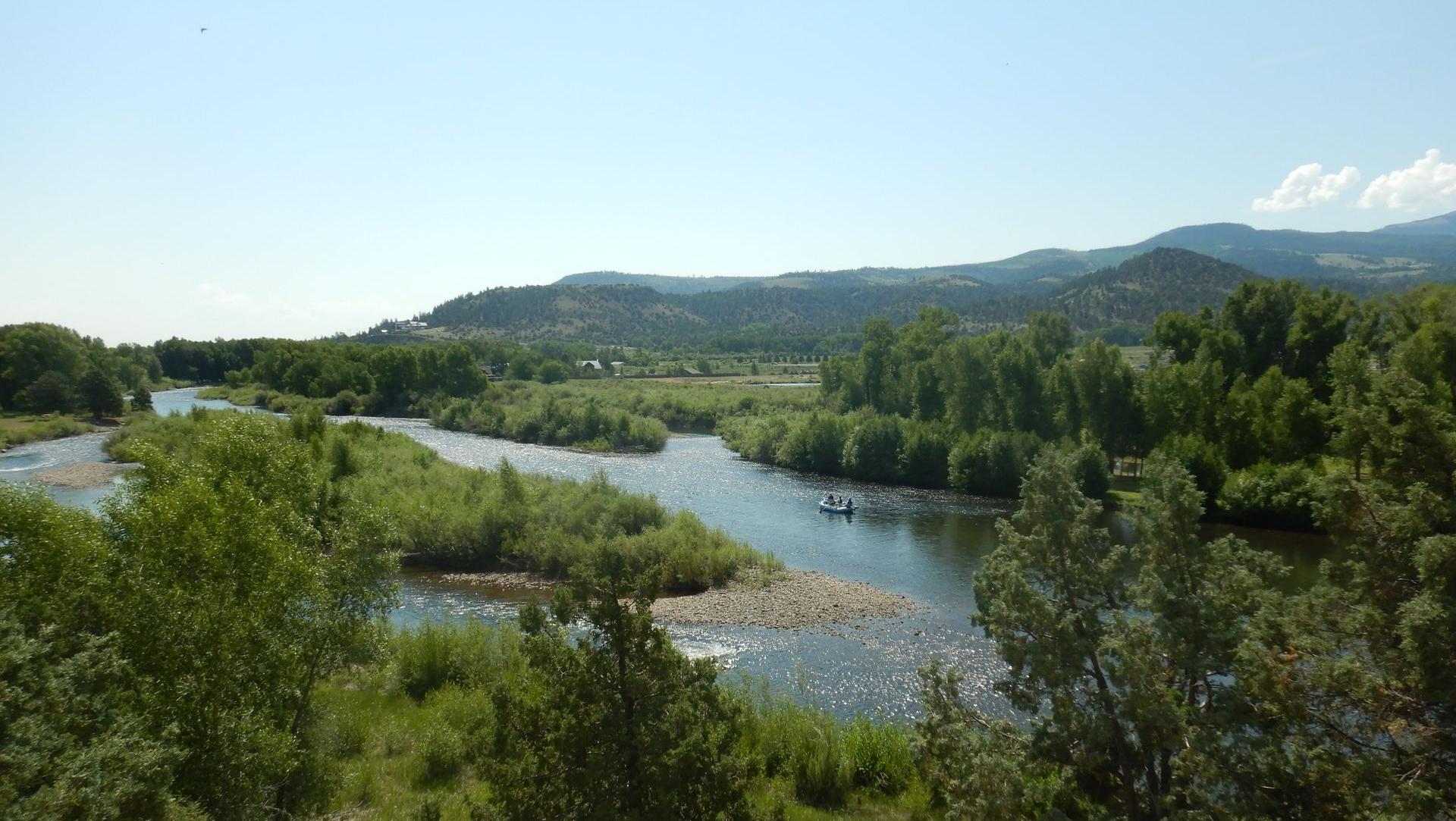 Wide river winding through a green valley with hills and trees under a clear blue sky