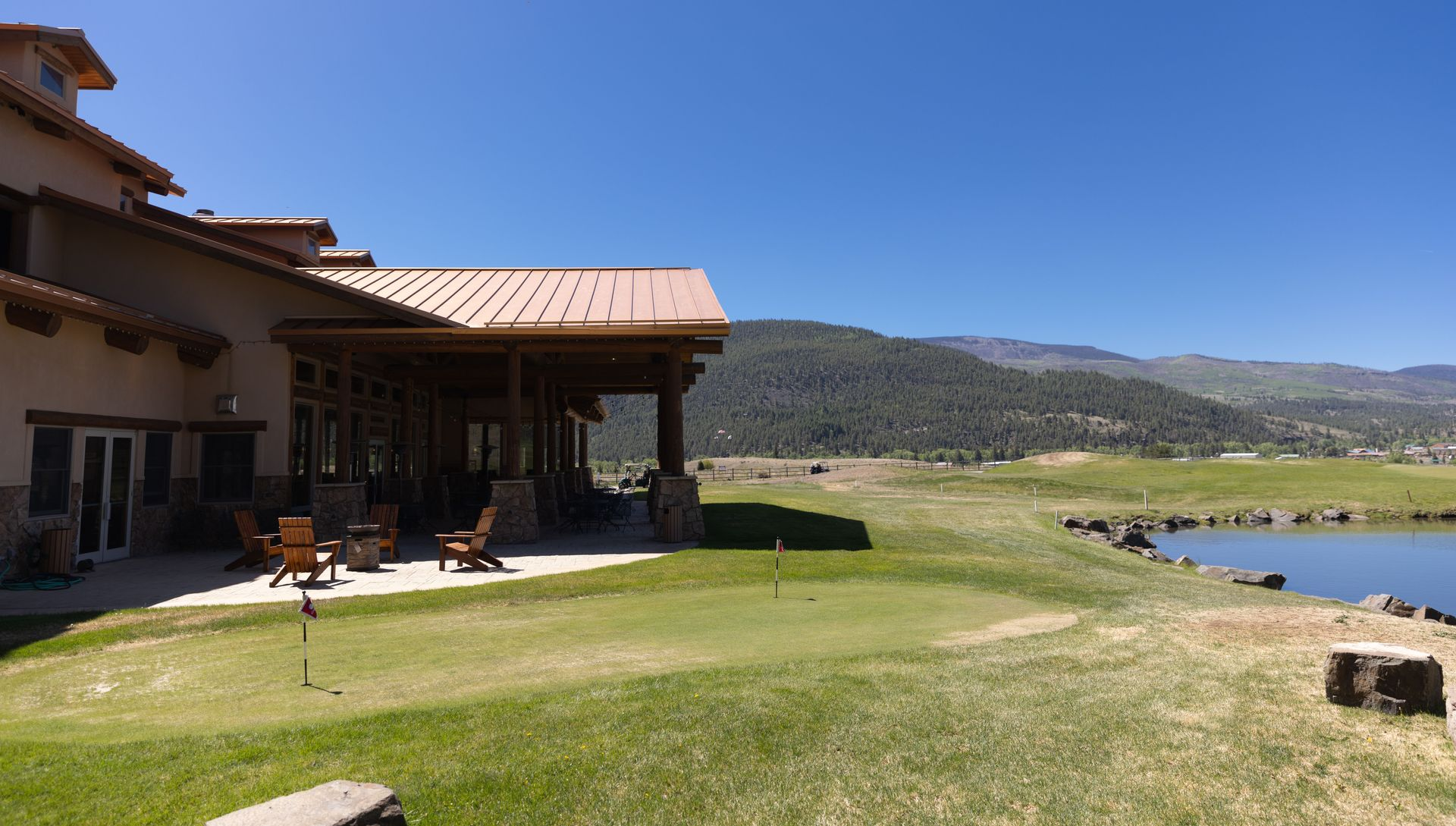 Lakeside patio beside a stucco house, with green lawn, hills, and blue sky.