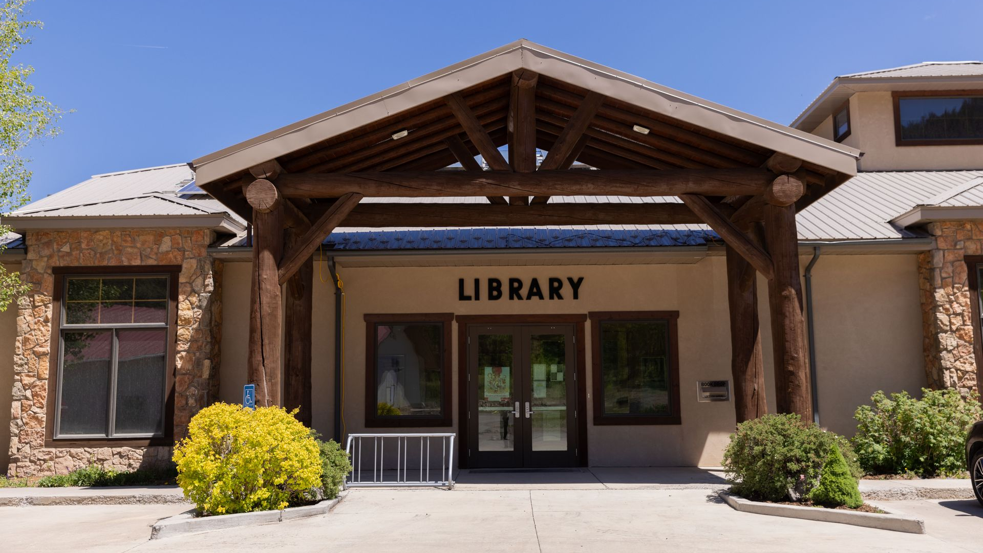 Library entrance with wooden beams and tan stucco building under a clear blue sky