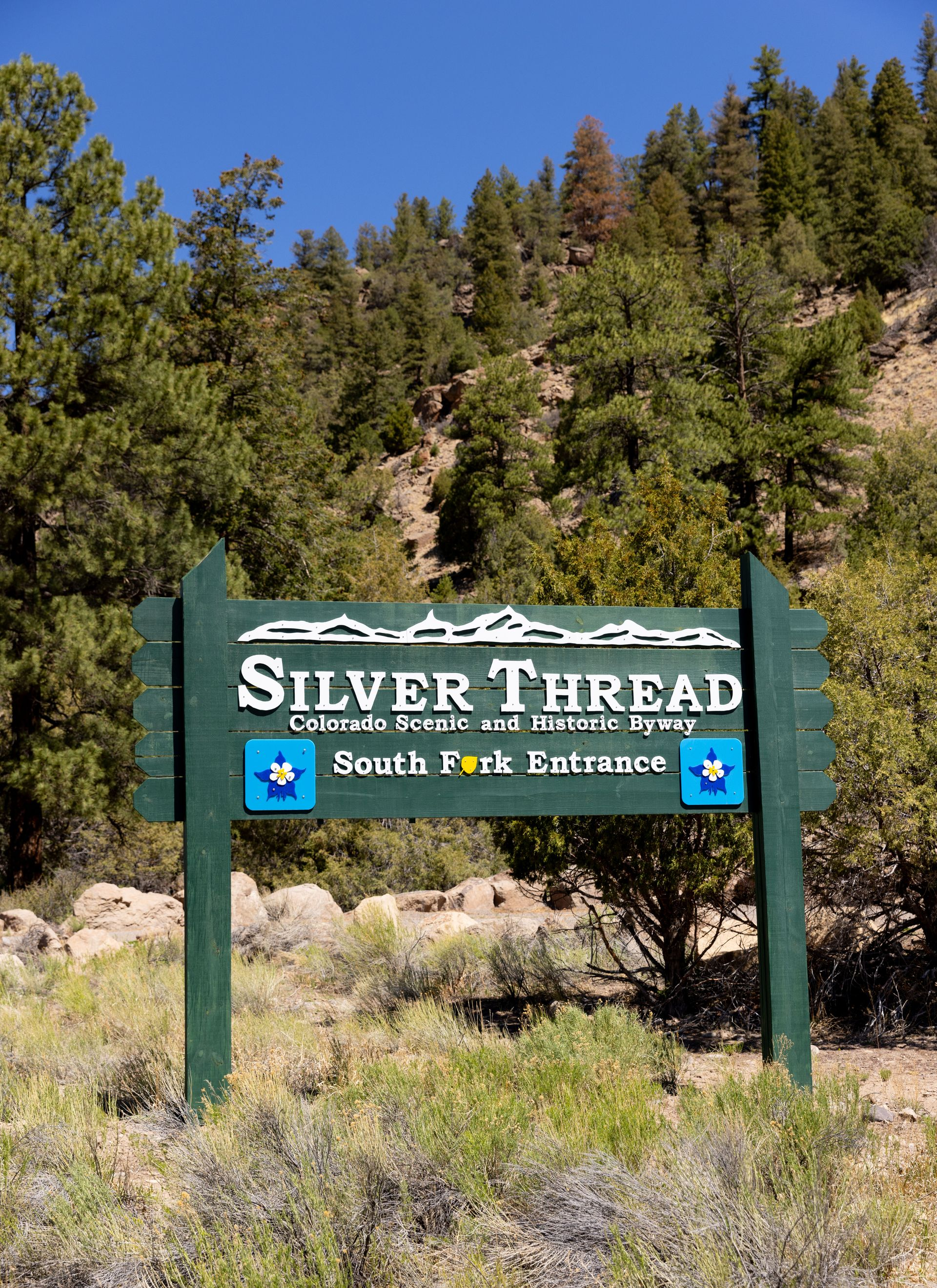 Green sign reading “Silver Thread” in a wooded mountain area.