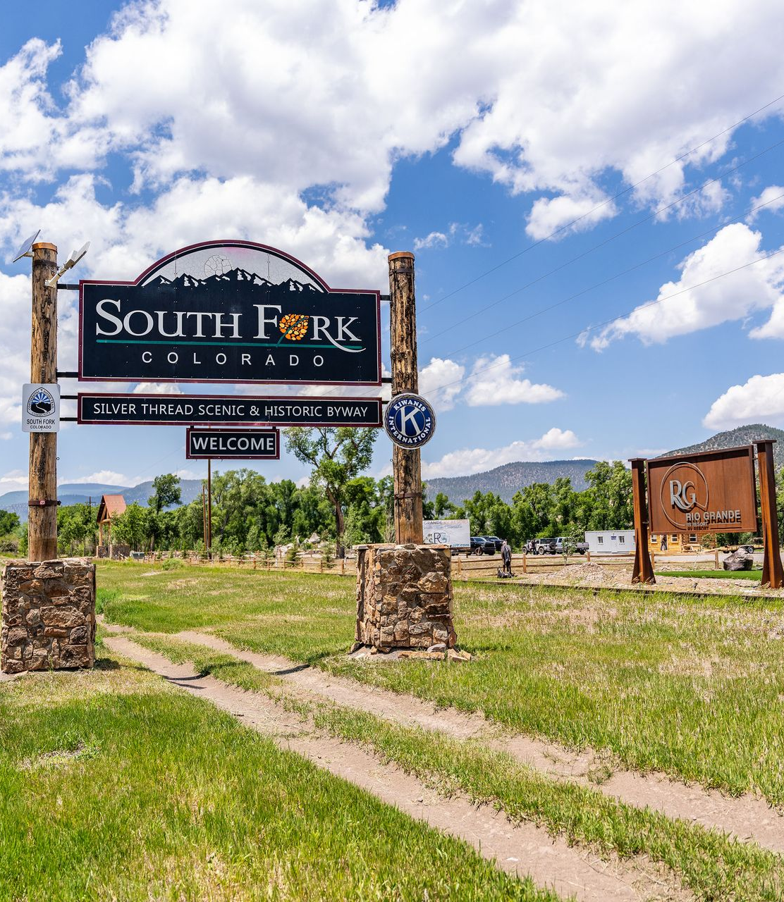South Fork Ranch entrance sign by a dirt road under a blue sky with clouds