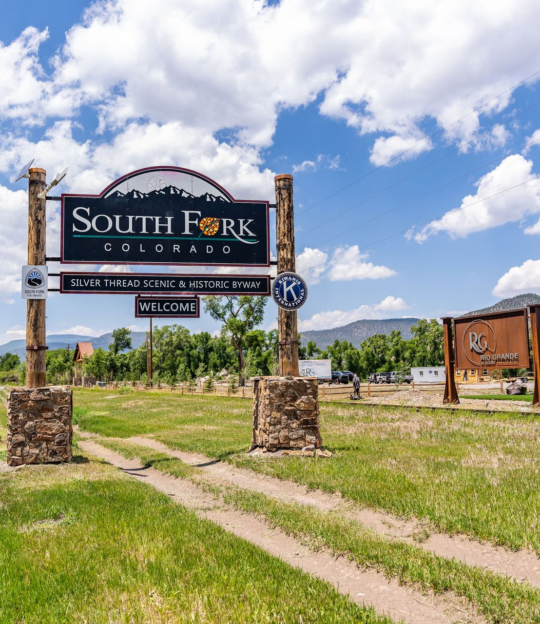 South Fork Colorado entrance sign beside a dirt path under a bright blue sky