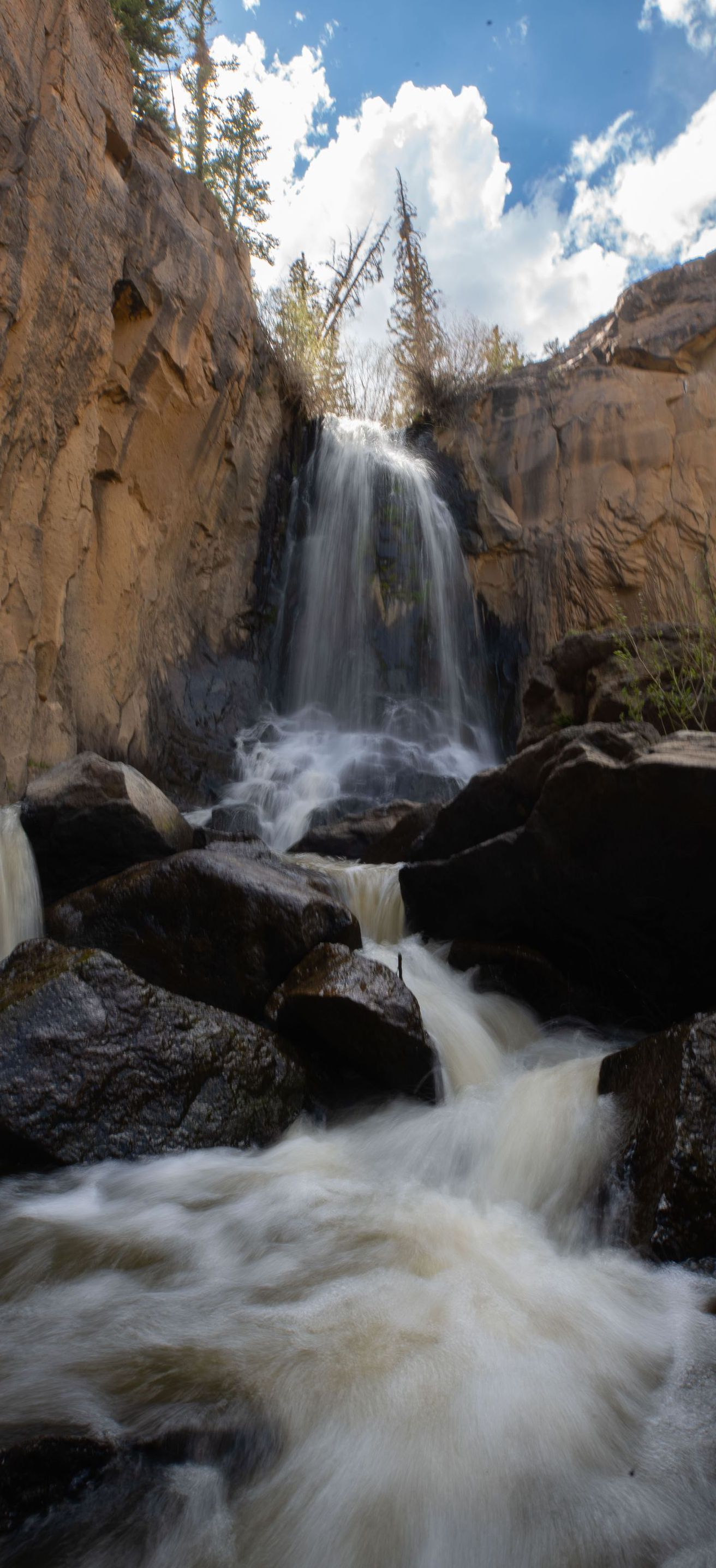 Waterfall cascading through a rocky canyon under a partly cloudy sky