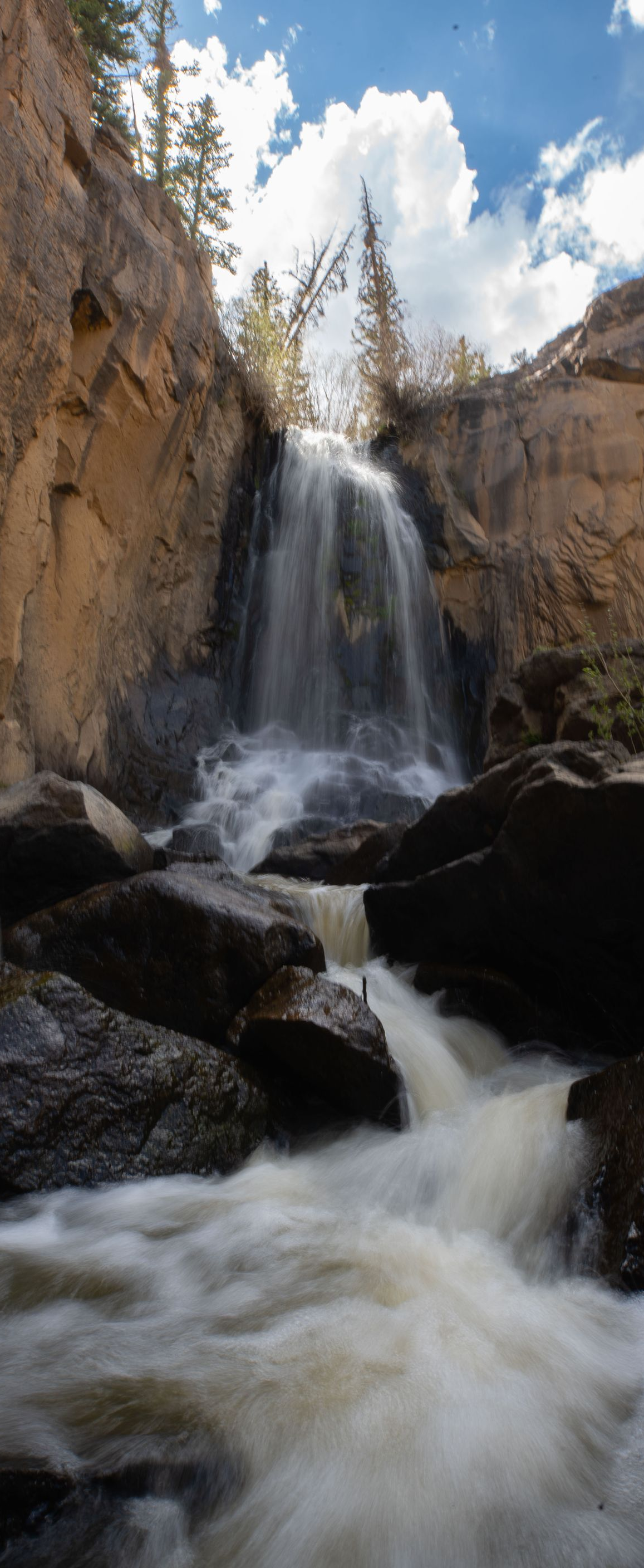 Waterfall cascading over rocky cliffs into a foamy river under a partly cloudy sky