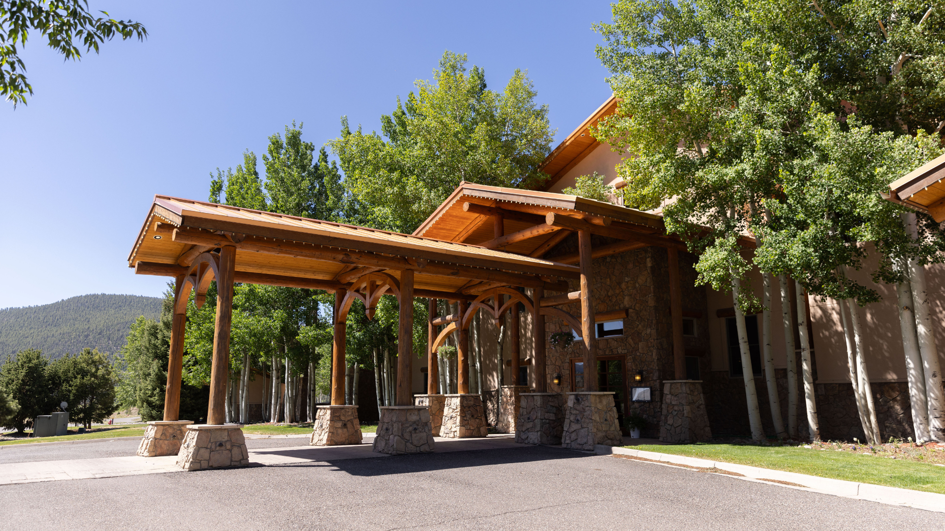 Wooden lodge entrance with covered walkway, stone pillars, and trees in bright daylight in Rio Grande RV Resort