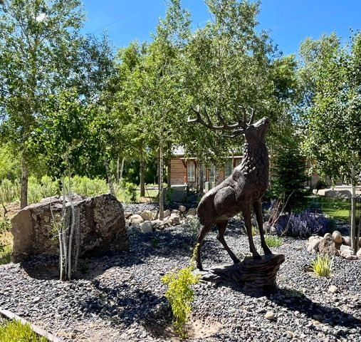 Bronze deer statue in a landscaped garden with rocks and trees under a blue sky