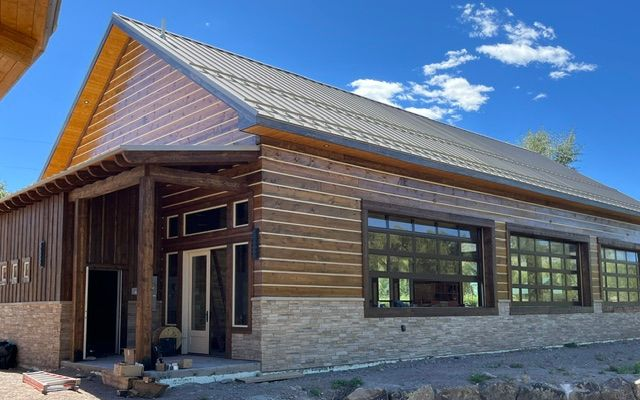 Modern wood-and-stone building exterior with large windows and a sloped metal roof under a blue sky