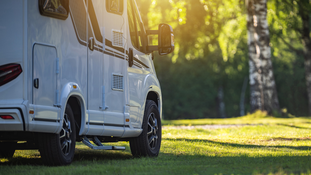 White RV parked on green grass, trees in background, sunny day.