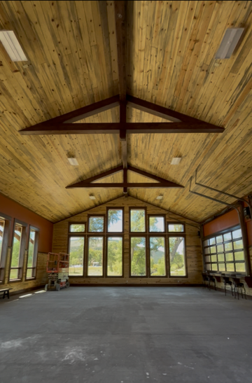 Empty rustic hall with wooden vaulted ceiling, large windows, and bare concrete floor