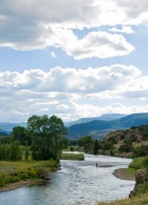 River winding through green valley under cloudy sky with distant mountains.