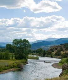 River winding through green valley under cloudy sky with distant mountains.