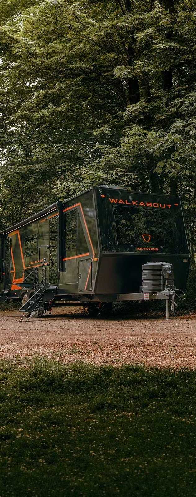 Camouflaged trailer or tiny cabin in a wooded campsite, with orange trim and a small deck