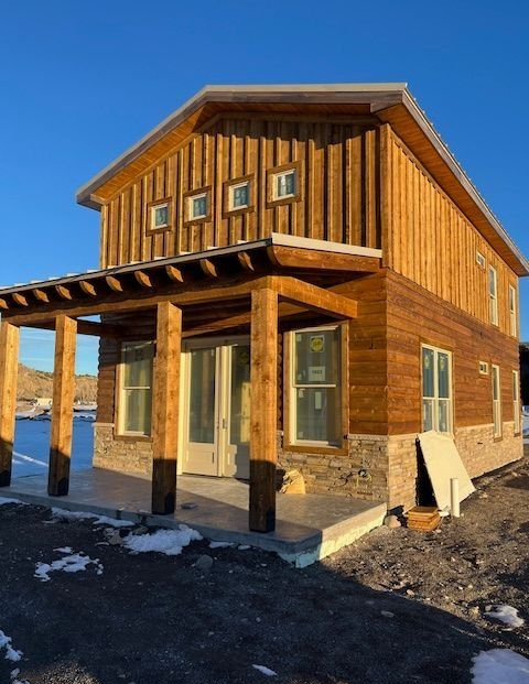 Two-story wooden house with a covered porch on a snowy, sunny lot