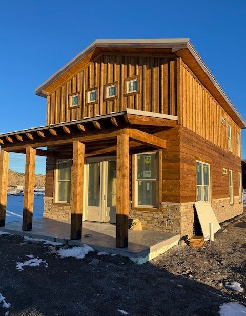 Wooden two-story house with a covered front porch in bright sunlight and patches of snow on the ground