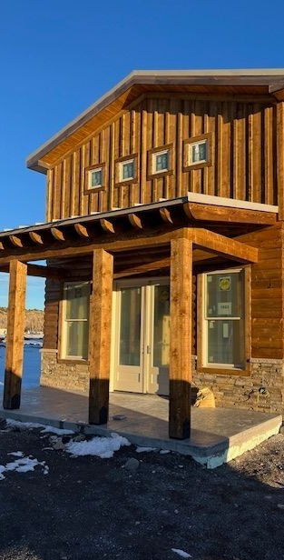 Rustic wooden building with stone base and covered porch in bright sunlight, snow on the ground