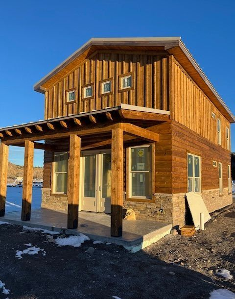 Wooden two-story house with porch and snow on the ground under a clear blue sky