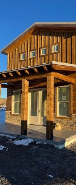 Sunlit rustic stone-and-wood house with covered porch and snowy ground