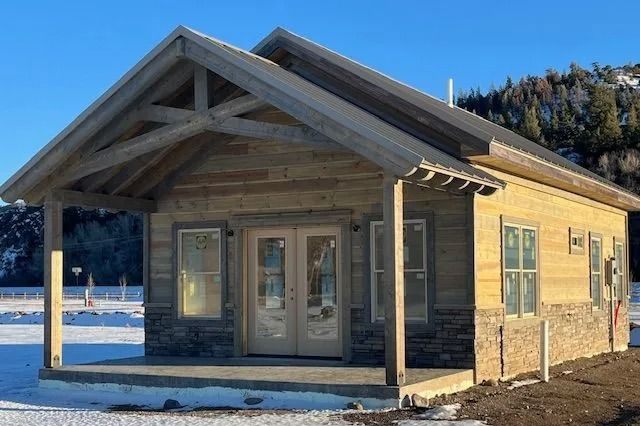 Small tan cabin with a porch and double doors in a snowy rural landscape.