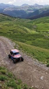 Off-road vehicle on a rocky mountain trail with green hills and distant peaks